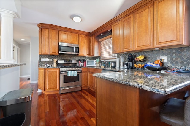 kitchen featuring stainless steel appliances, tasteful backsplash, dark hardwood / wood-style flooring, kitchen peninsula, and dark stone countertops