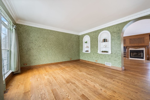 empty room with hardwood / wood-style flooring, built in features, plenty of natural light, and crown molding