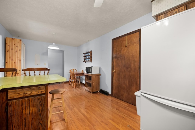 kitchen featuring light hardwood / wood-style flooring, a textured ceiling, decorative light fixtures, white appliances, and a breakfast bar