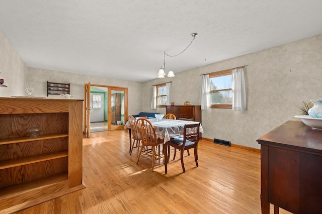 dining area featuring french doors, light wood-type flooring, a textured ceiling, and an inviting chandelier