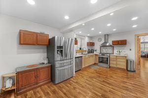 kitchen with wall chimney range hood, stainless steel appliances, and light hardwood / wood-style flooring