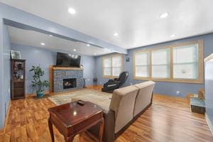 living room with beam ceiling, a stone fireplace, and light wood-type flooring