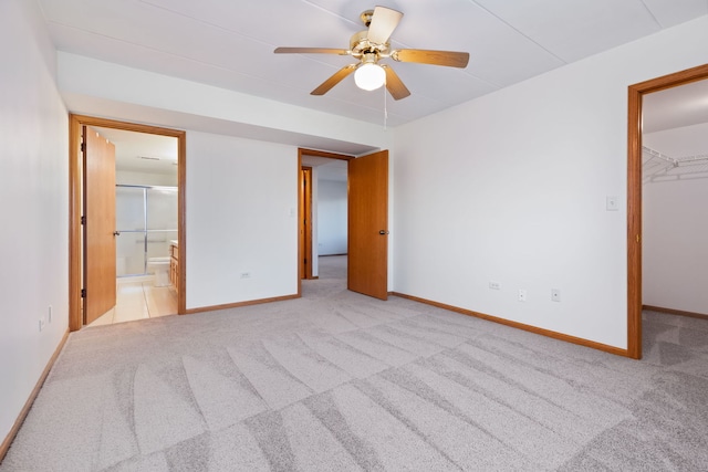 unfurnished bedroom featuring ensuite bathroom, a walk in closet, light carpet, a closet, and ceiling fan