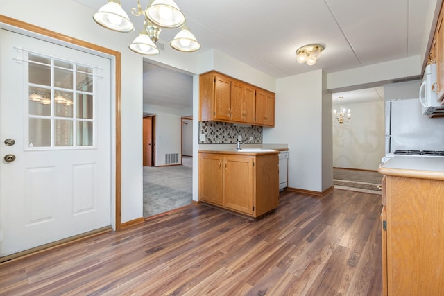 kitchen featuring a notable chandelier, white appliances, hanging light fixtures, backsplash, and dark hardwood / wood-style floors