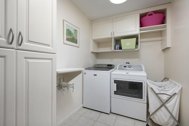 clothes washing area featuring cabinets, light tile patterned floors, and washing machine and clothes dryer