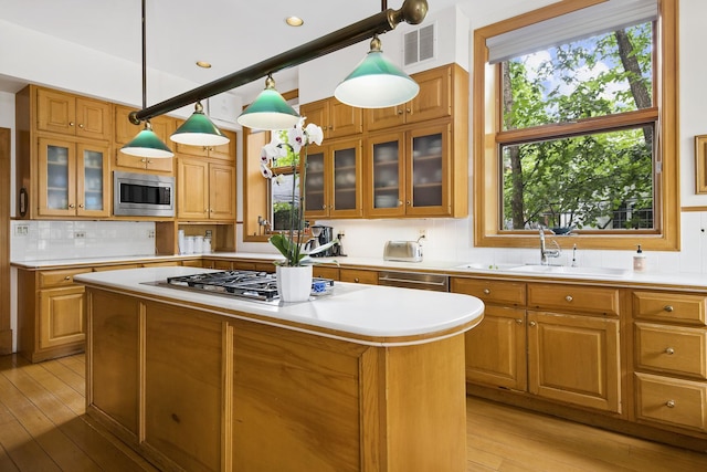 kitchen with appliances with stainless steel finishes, light wood-type flooring, sink, pendant lighting, and a kitchen island