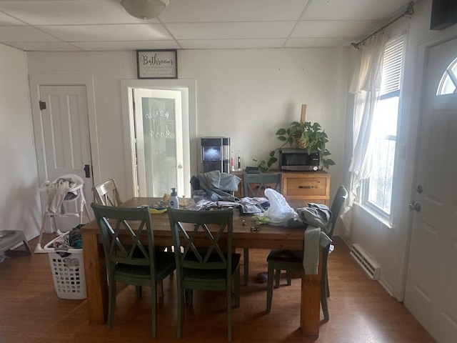 dining room with a baseboard heating unit, hardwood / wood-style flooring, a healthy amount of sunlight, and a paneled ceiling