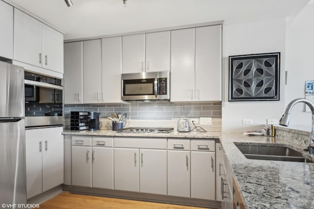 kitchen featuring light stone countertops, light hardwood / wood-style flooring, backsplash, appliances with stainless steel finishes, and sink