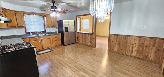 kitchen with stainless steel refrigerator with ice dispenser, ceiling fan with notable chandelier, gas stove, sink, and light hardwood / wood-style floors