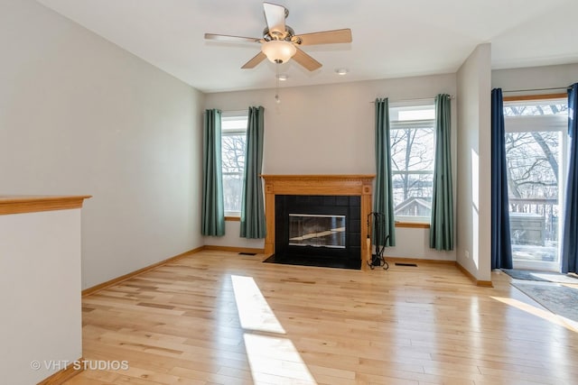 unfurnished living room with a tiled fireplace, a wealth of natural light, and light hardwood / wood-style floors