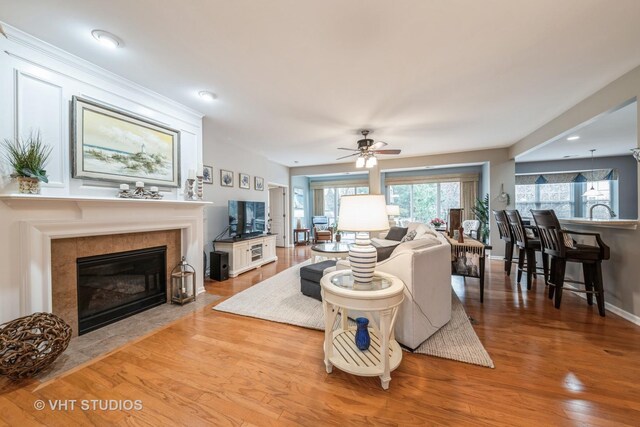 living room featuring light hardwood / wood-style floors, ceiling fan, and a tiled fireplace