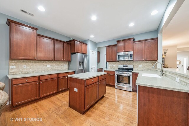 kitchen featuring backsplash, ceiling fan, appliances with stainless steel finishes, light hardwood / wood-style floors, and kitchen peninsula