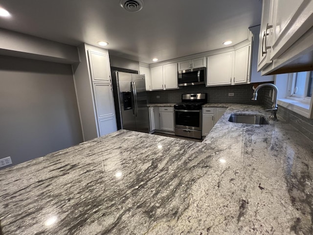 kitchen with decorative backsplash, stainless steel appliances, sink, dark stone countertops, and white cabinets