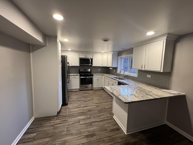 kitchen featuring kitchen peninsula, appliances with stainless steel finishes, light stone counters, sink, and white cabinetry