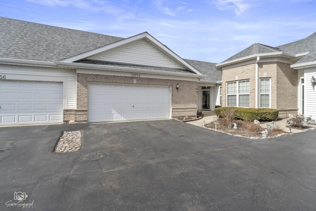 single story home featuring driveway, brick siding, and roof with shingles