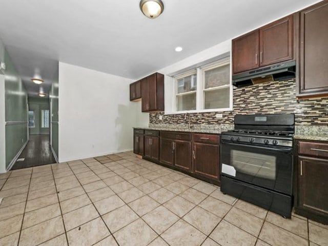 kitchen with tasteful backsplash, light stone counters, black range with gas stovetop, sink, and light tile patterned floors