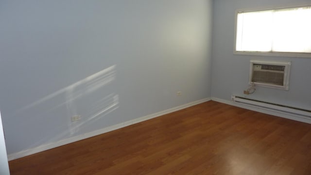 empty room with a wall mounted air conditioner, hardwood / wood-style floors, and a baseboard radiator