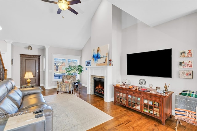 living room with a fireplace, ornate columns, hardwood / wood-style floors, ceiling fan, and high vaulted ceiling