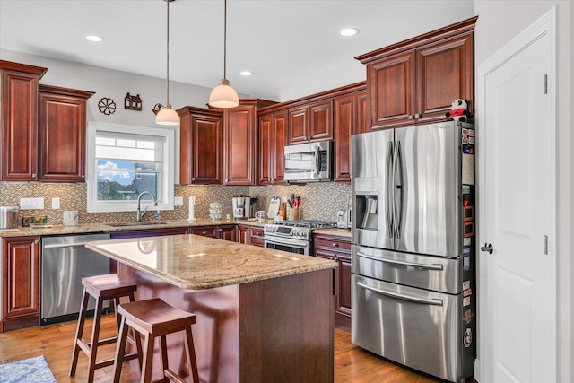 kitchen featuring appliances with stainless steel finishes, a kitchen bar, a kitchen island, sink, and decorative light fixtures