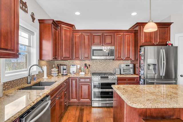 kitchen featuring appliances with stainless steel finishes, hanging light fixtures, dark hardwood / wood-style flooring, light stone counters, and sink