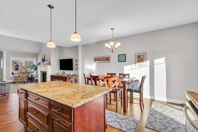 kitchen with a center island, light wood-type flooring, light stone countertops, pendant lighting, and a notable chandelier