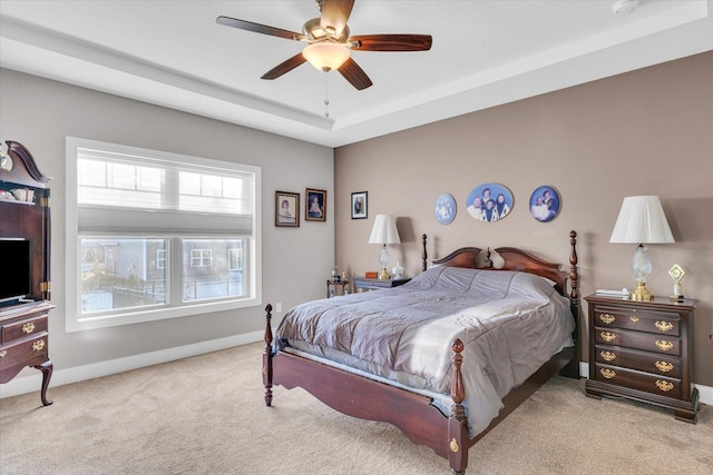 bedroom featuring ceiling fan, a tray ceiling, and light carpet