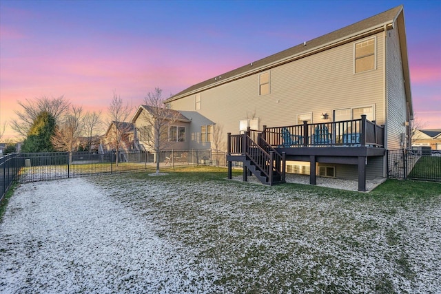 back house at dusk featuring a wooden deck and a lawn