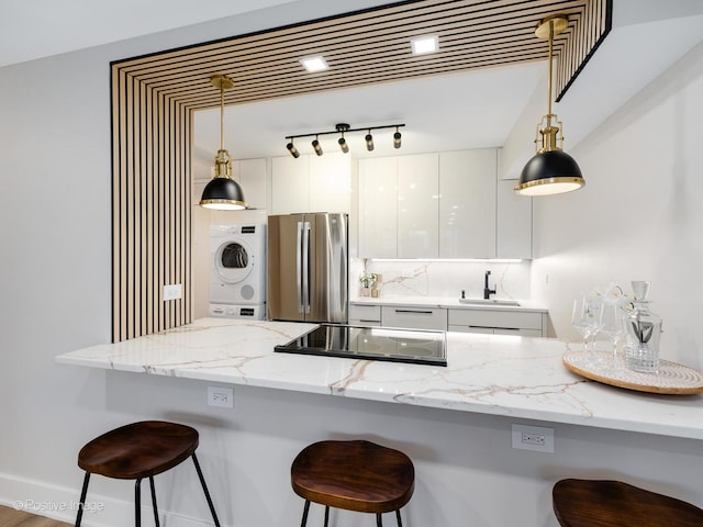 kitchen featuring stainless steel refrigerator, white cabinetry, hanging light fixtures, stacked washer / dryer, and a breakfast bar area