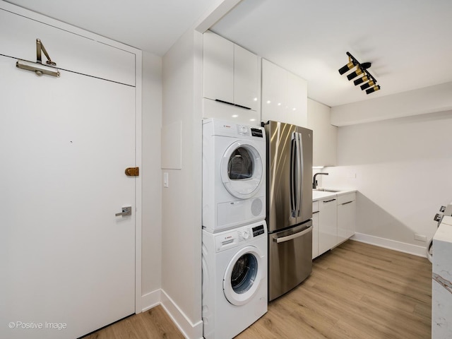 clothes washing area with stacked washer and dryer, light wood-type flooring, and sink