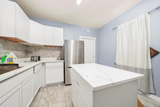 kitchen featuring a kitchen island, decorative backsplash, white cabinetry, and stainless steel fridge