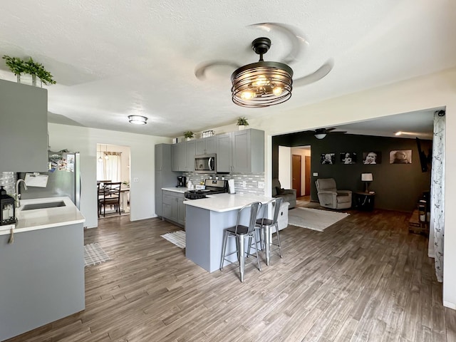 kitchen featuring kitchen peninsula, appliances with stainless steel finishes, backsplash, ceiling fan, and gray cabinets