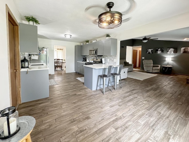 kitchen featuring kitchen peninsula, appliances with stainless steel finishes, light hardwood / wood-style floors, a breakfast bar, and gray cabinets