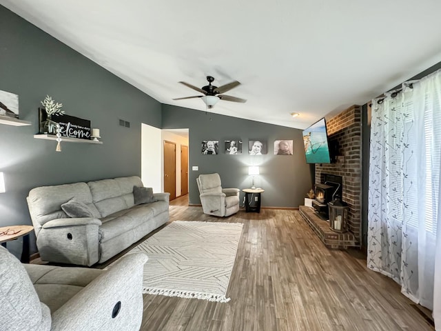 living room featuring hardwood / wood-style floors, lofted ceiling, ceiling fan, and a wood stove