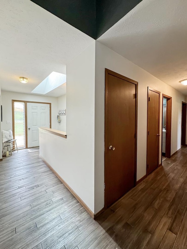 hall with a skylight, a textured ceiling, and hardwood / wood-style flooring