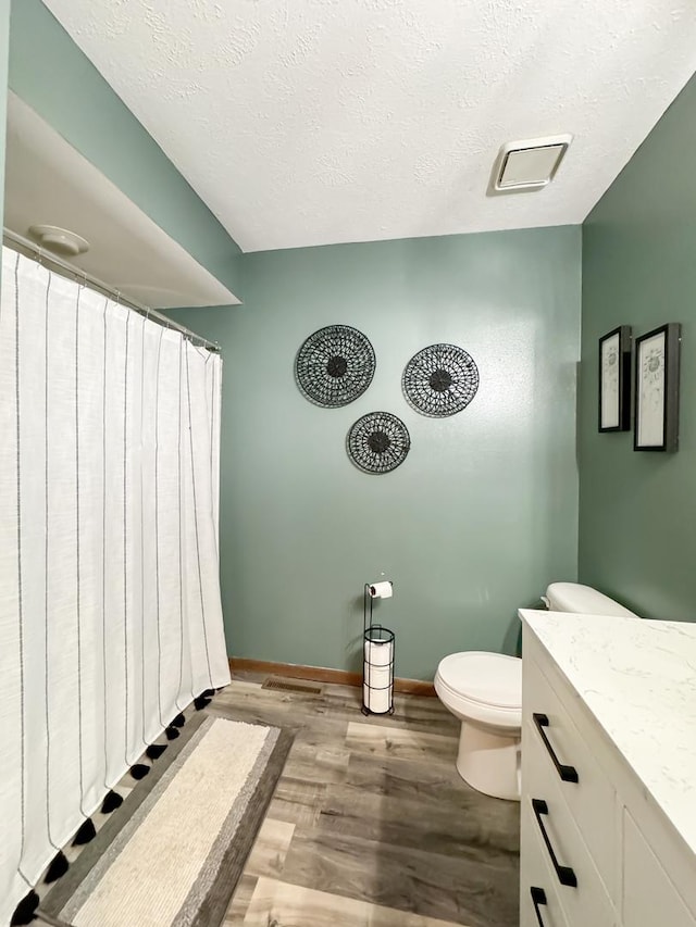 bathroom featuring vanity, wood-type flooring, a textured ceiling, and toilet