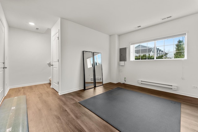 workout room featuring hardwood / wood-style floors, electric panel, and a baseboard heating unit