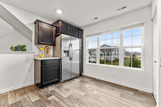 kitchen featuring dark brown cabinets, stainless steel fridge, light stone counters, and light hardwood / wood-style floors