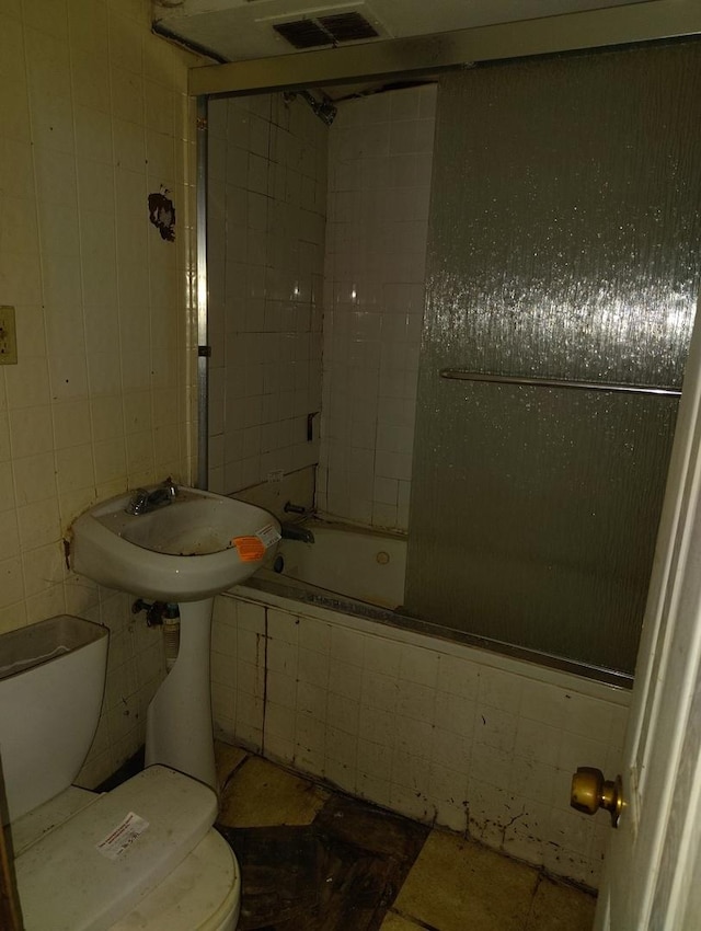 bathroom featuring tub / shower combination, toilet, and tile walls