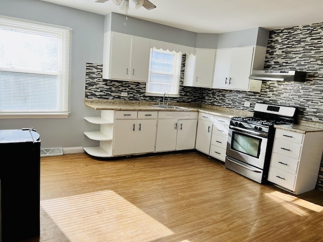 kitchen featuring ventilation hood, stainless steel range with gas cooktop, sink, light wood-type flooring, and white cabinetry