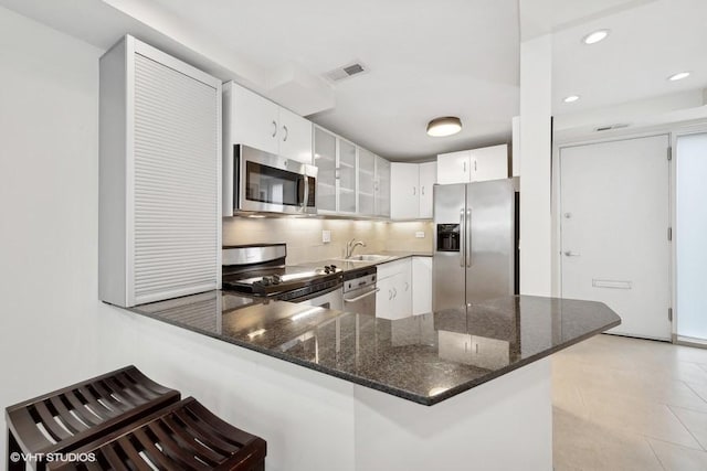 kitchen featuring white cabinets, appliances with stainless steel finishes, a kitchen bar, sink, and kitchen peninsula