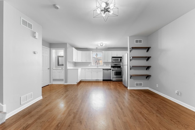 kitchen featuring appliances with stainless steel finishes, white cabinetry, an inviting chandelier, light hardwood / wood-style floors, and hanging light fixtures