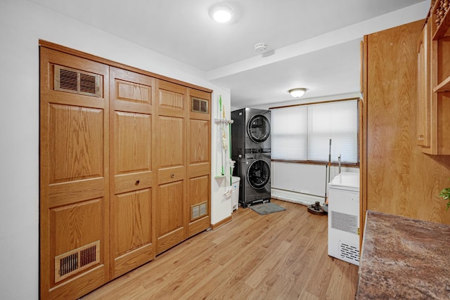 laundry area with light hardwood / wood-style flooring and stacked washing maching and dryer