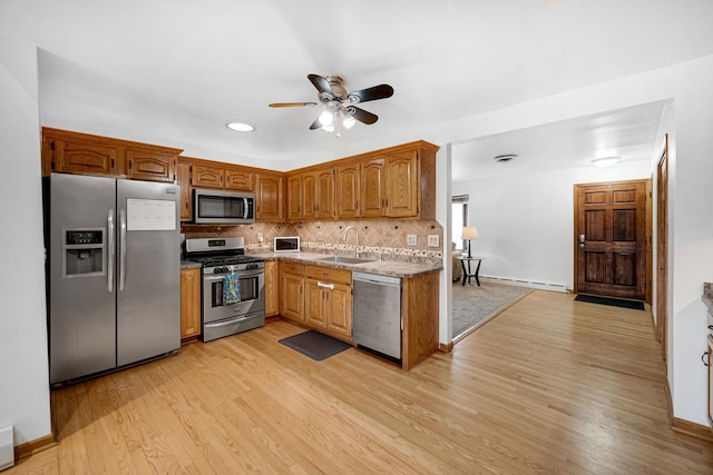 kitchen with decorative backsplash, appliances with stainless steel finishes, baseboard heating, sink, and light hardwood / wood-style floors