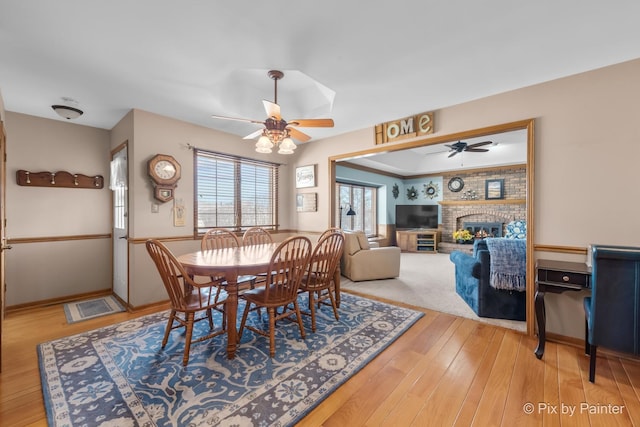 dining room featuring hardwood / wood-style flooring, ceiling fan, and a brick fireplace