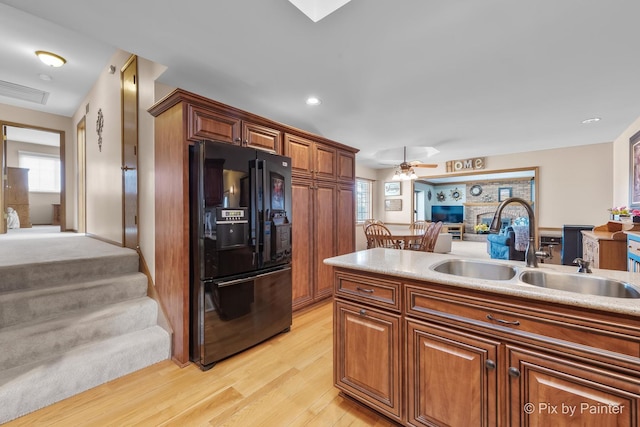 kitchen with black fridge with ice dispenser, light hardwood / wood-style floors, ceiling fan, and sink