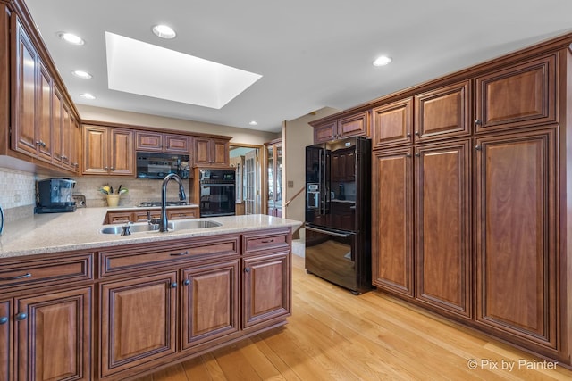 kitchen with black appliances, sink, a skylight, decorative backsplash, and light wood-type flooring