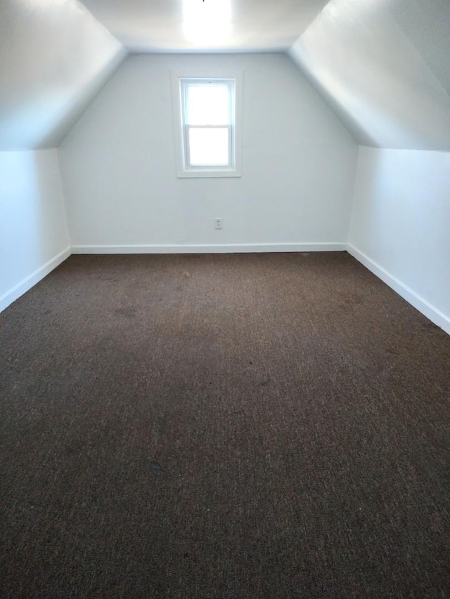 bonus room with dark carpet and vaulted ceiling