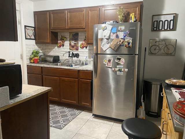 kitchen with stainless steel fridge, backsplash, dark brown cabinets, sink, and light tile patterned floors