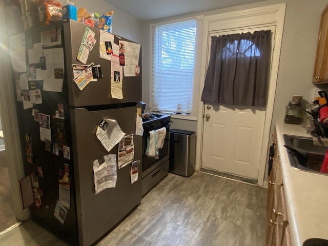 kitchen with black gas range, sink, and stainless steel refrigerator