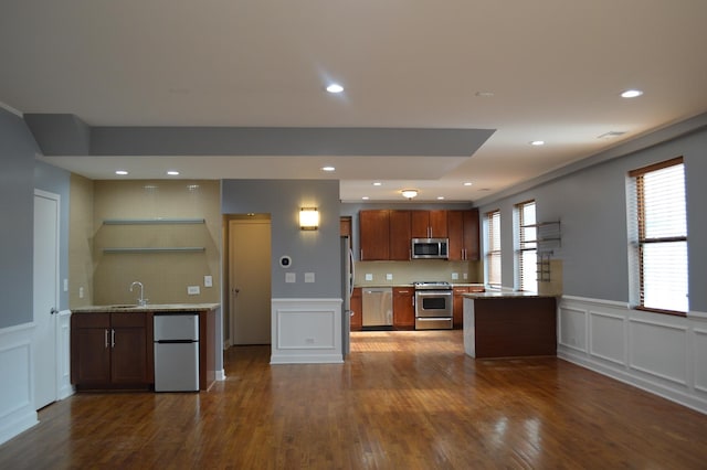 kitchen featuring sink, appliances with stainless steel finishes, dark hardwood / wood-style flooring, light stone counters, and kitchen peninsula